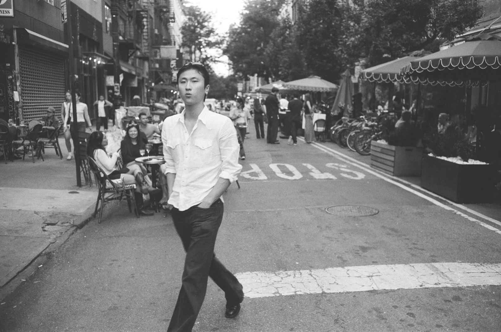 Man in a white shirt crossing a street, looking directly into the camera, black-and-white street photograph, New York City